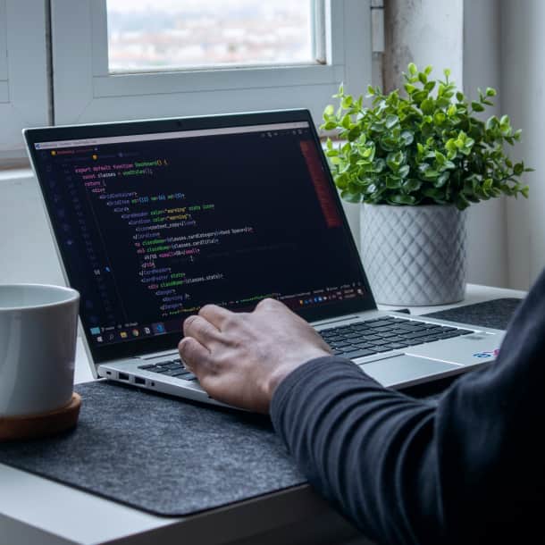 A person writing code on his laptop on a white desk
