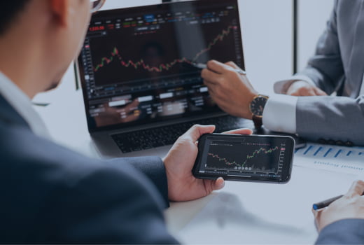 People monitoring financial charts on a laptop and a phone