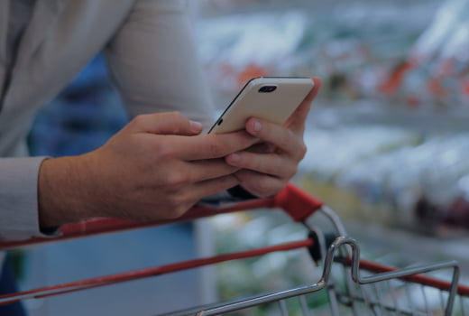 A person with a phone pushing a trolley in a supermarket