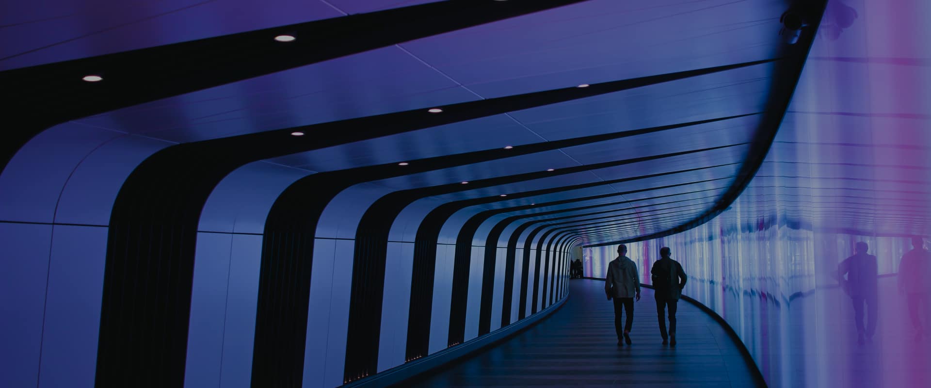 Two people pass through a corridor surrounded by a glass wall