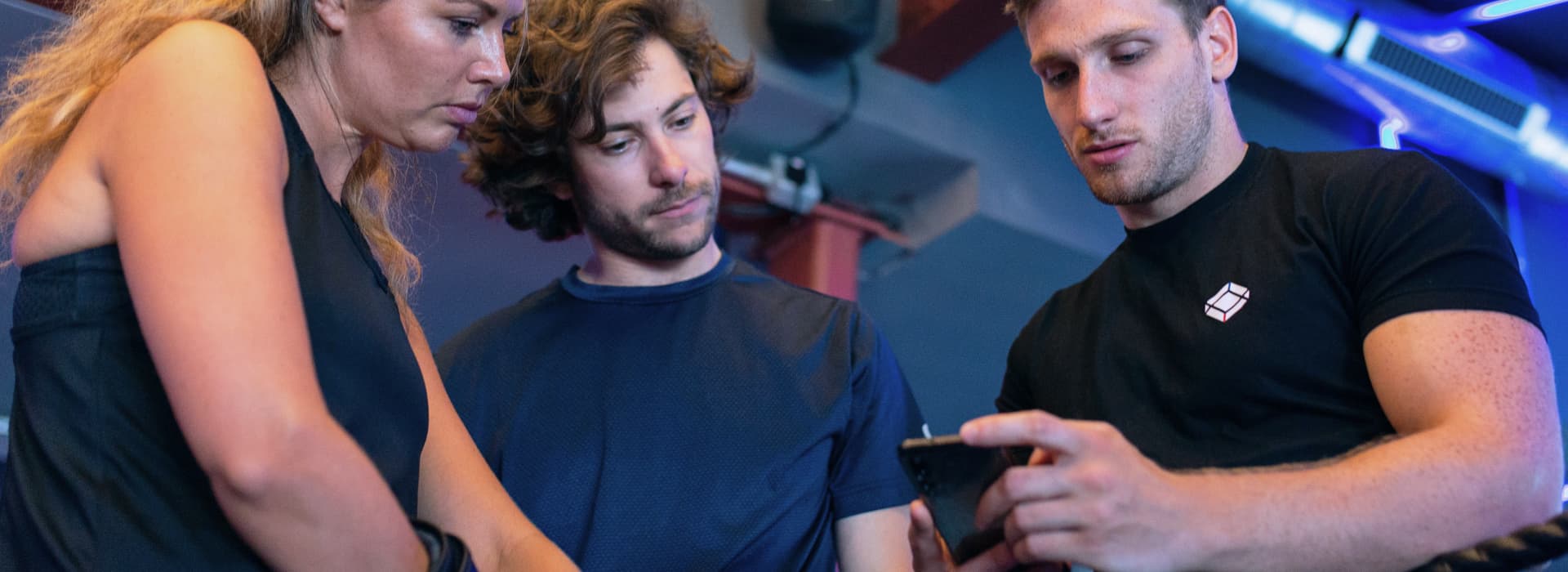 Three people in fitness suits looking at a phone screen