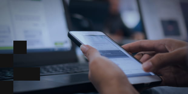 A person hold a mobile phone in front of a laptop monitor