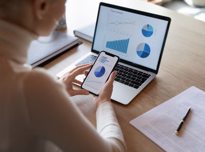 A person monitoring real estate graphics on a mobile  phone and a laptop