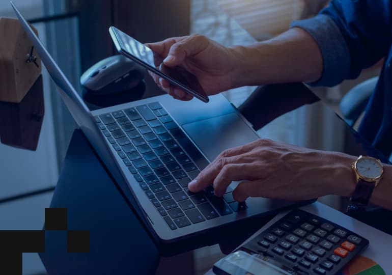 A person operating fintech apps on a laptop and mobile phone