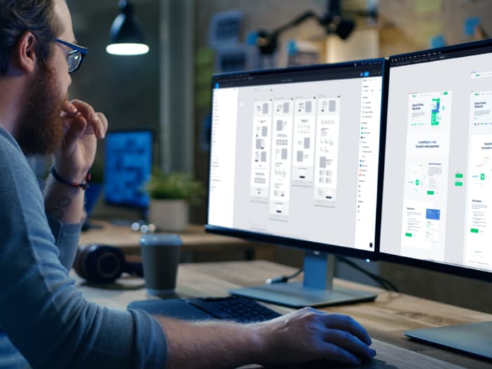 A person designing a web page on two monitors